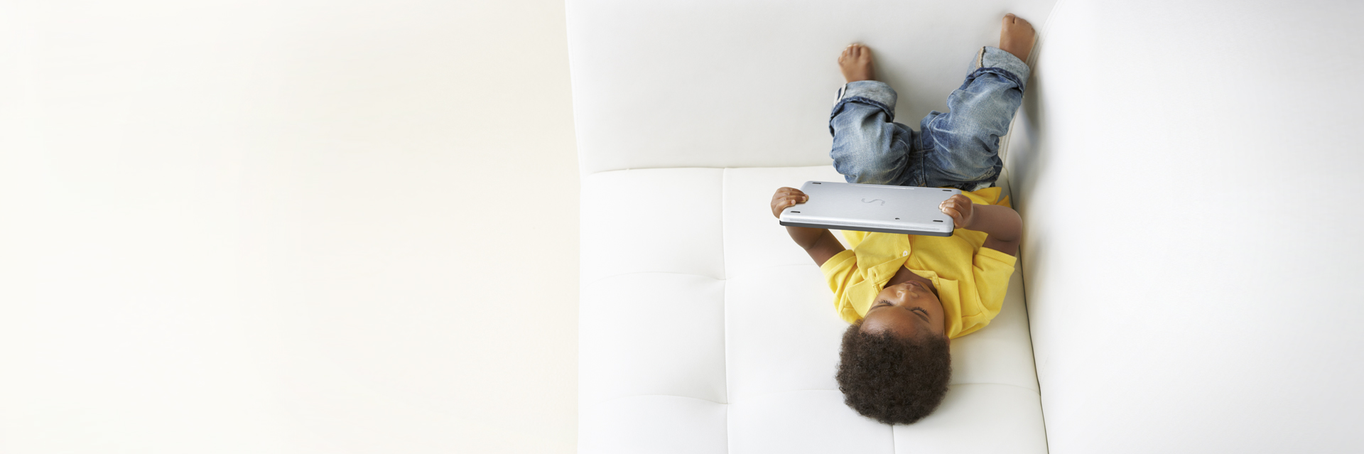 La photo représente un enfant allongé sur un canapé en train de regarder la tablette.