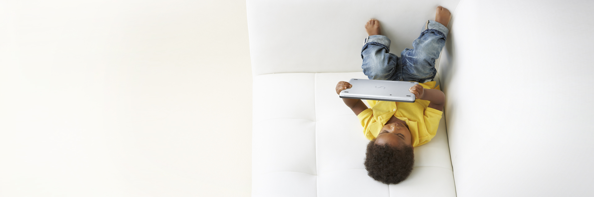 The picture shows a child lying on a sofa looking at the tablet.