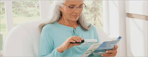 La photo représente une dame utilisant la loupe Mobilux Led pour lire un magazine